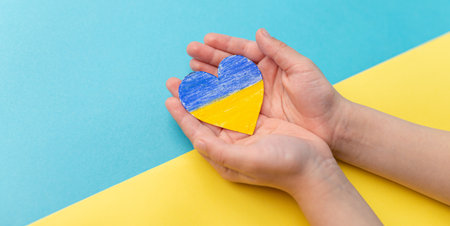 The concept of ending the war in Ukraine. Heart in the colors of the flag of Ukraine in child hands