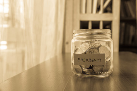 A savings money jar with world coins and emergency word on label or tagの写真素材