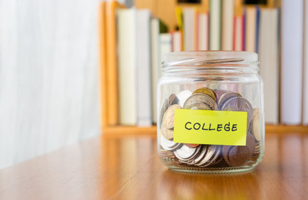 Many world coins in saving money jar with college label on jar, concept to financial planning for kidsの写真素材
