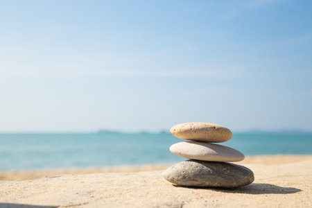 Stones balance, pebbles stack on the sand beach with shadow on right side , beautiful sea view during daytime on a sunny day with blue sky on backgroundの写真素材