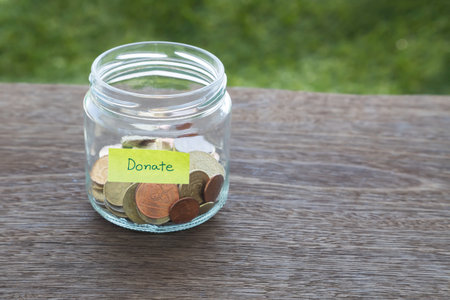 World coins in money glass jar with DONATE word label place on natural wood table, blank space for textの写真素材