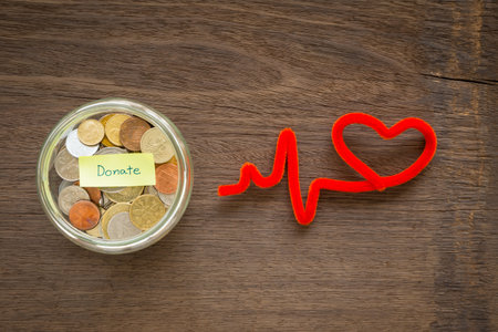 Top view of world coins in money glass jar with DONATE word label and red heart shape craft place on natural wood backgroundの写真素材