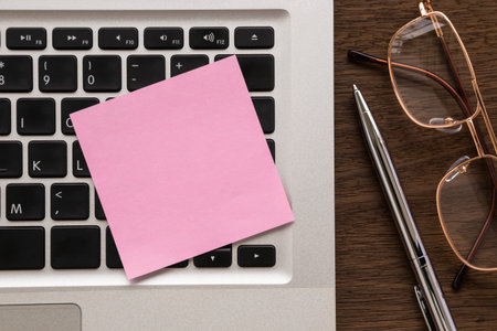 Blank pink notepad putting on laptop. pen and eye glasses on wood table
