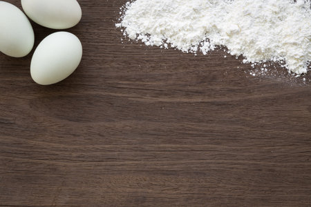 Top view of baking background with eggs and flour on vintage natural wood table. Rough texture and...