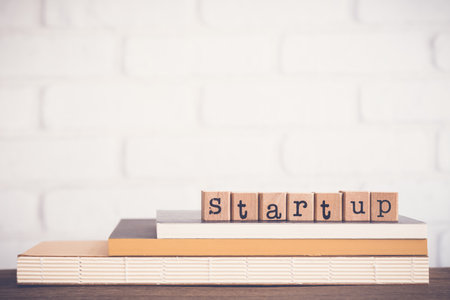 The word Startup, alphabet on wooden rubber stamps on top of books and table.  Background copy space, vintage minimal style. Creative ideas, initiate innovation, future careers, business concepts.の写真素材