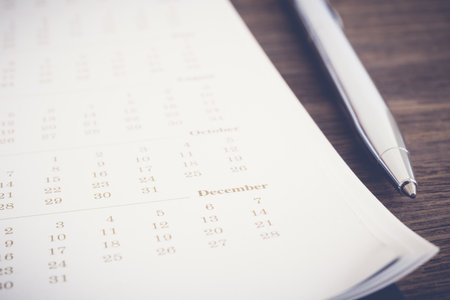 Closeup calendar pages focus on December month, blurred dates pass, modern pen put beside on wooden table. Brown tone vintage minimal style. Vision, schedule project planning, business agenda review.の写真素材