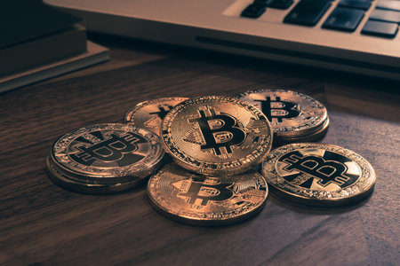 Close up gold Bitcoins on wooden table, notebook in background with dark room light, vintage retro...