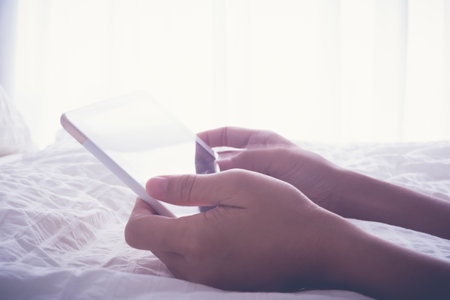 Woman hands hold and touch on tablet screen while lying down on bed, white duvet on background and...