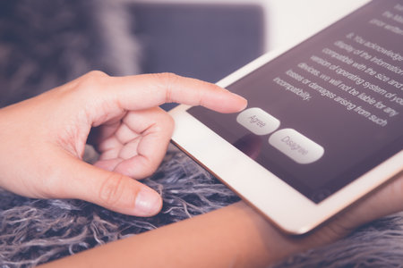 Closeup woman hands using device, finger click or point at Agree button on tablet screen while reading application, customer or business information. Living room, lifestyle, vintage and retro.の写真素材