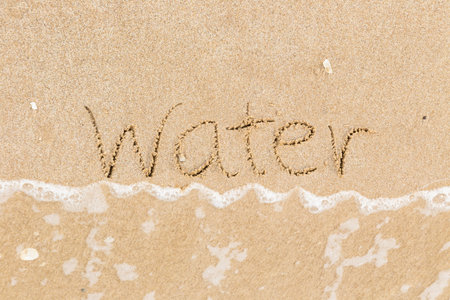 Top view of the word Water written in sand beach with foam wave in background, Natural daylight in summer season. Texture, saving environment concepts.の写真素材