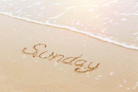 The word Sunday written in sand beach with sunlight reflex and wave in background, bird eye view. Outdoor picture in summer season. Day, weekend, travel and relaxation concepts.の写真素材