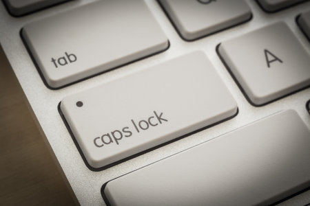 Close up caps lock button on white keyboard, wooden table on background, dark filter. Computer...