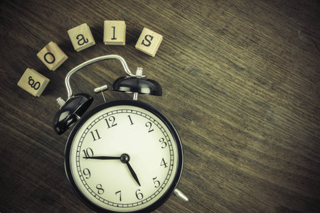 Goals word concept with alarm clock on wooden table texture background, blank space. Text on wooden cube block stampers, vintage retro and flat lay style. Business management ideas.の写真素材