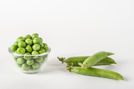 Fresh shelled green peas in a glass bowl and whole peas on whiteの写真素材