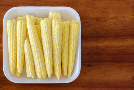 Dish containing a stack of baby corn cobs on a wooden backgroundの写真素材
