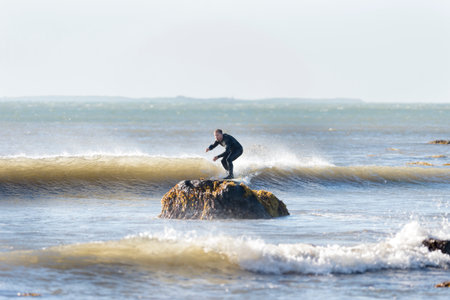 Westport, Massachusetts, USA - July 5, 2014: Surfer off Gooseberry Neck appears to be riding small wave into a rock. Buzzards Bay and Cuttyhunk Island in background.のeditorial素材