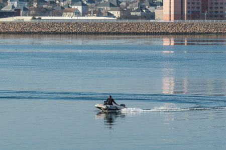 New Bedford, Massachusetts, USA - March 30, 2019: Man and dog in small inflatable boat making u-turn...