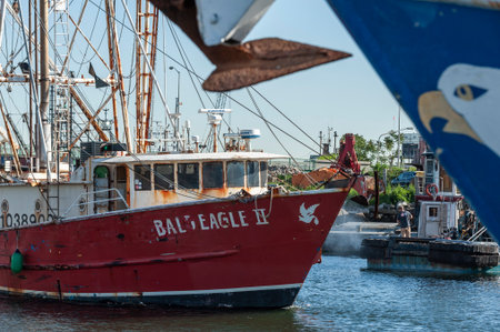 New Bedford, Massachusetts, USA - June 8, 2019: Man pressure washing work boat as commercial fishing vessel Bald Eagle II eases her way up channel on Acushnet Riverのeditorial素材