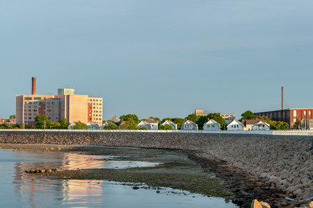 Densely populated neighborhood of homes, apartments and old factories behind hurricane barrier in New Bedford, Massachusetts, USA, with Acushnet River at low tide in foregroundのeditorial素材