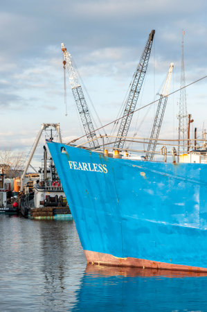 New Bedford, Massachusetts, USA - March 15, 2018: Bow of fishing vessel Fearless with cranes and tugs in backgroundのeditorial素材