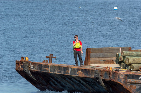 New Bedford, Massachusetts, USA - June 8, 2018: Crewman thumbs walkie-talkie as barge is pushed toward gap in New Bedford hurricane barrierのeditorial素材