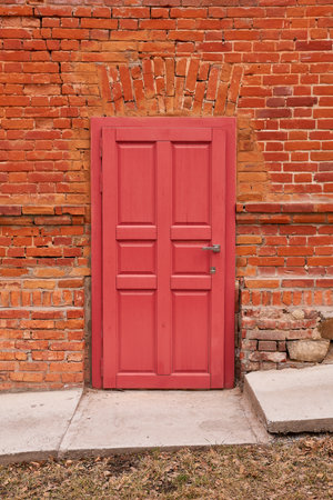 A red door in a cracked brick wall, next to a concrete walkwayの写真素材