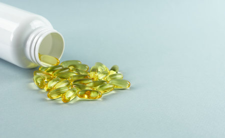 Omega-3 capsules are scattered on a blue background next to a white bottle.の写真素材