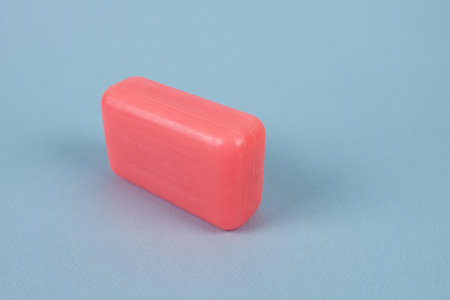 A piece of pink soap on a blue background. Hygiene product.