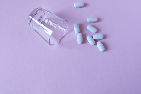 Pills spilling out of a glass with pills on a colored background. Place for copying text.の写真素材