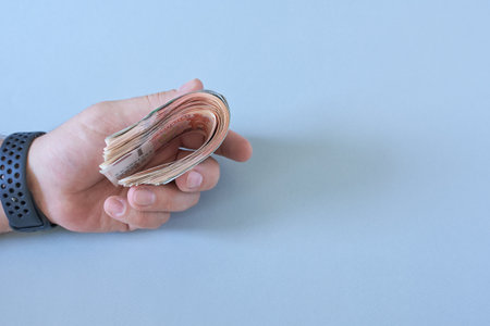 Male hand with bills on blue background with blank space for text.の写真素材
