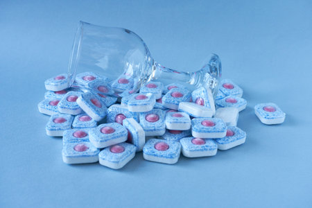 Dishwasher tablets and wine glass on blue background. Clean dishes concept.の写真素材