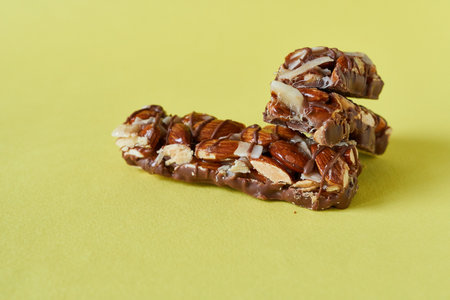 Nut bars with chocolate on yellow background. Close-up.