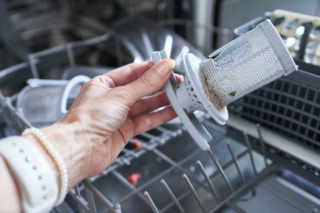 Broken dishwasher. Close-up of a woman's hand and a broken dishwasher filter.の写真素材