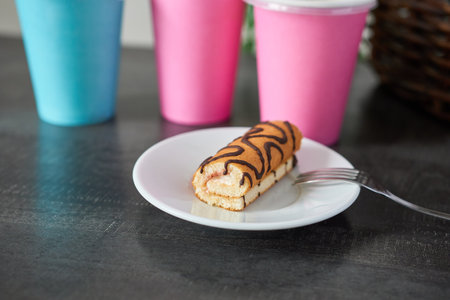 Biscuit roll on a white plate and paper cups on the table. A snack at the cafÃ©.
