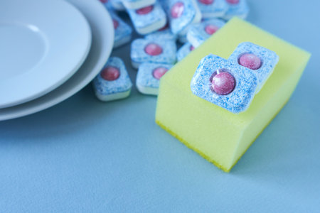 Dishwasher tablets in front of clean dishes. Dishwasher tablets and sponge.
