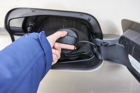 Close-up of a woman's hand opening a petrol tank cap in a car.