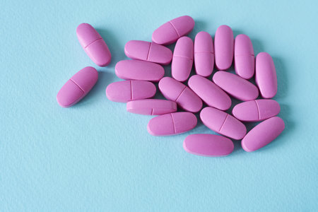 Pink pills isolated on blue background. Top view. Copy space.の写真素材