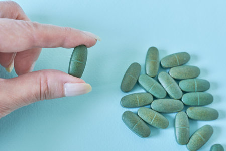 Woman hand holding green pills on blue background. Healthcare and medical concept.