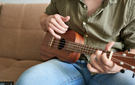 Young man playing ukulele on sofa at home, closeup