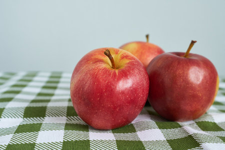 Three red apples on a green tablecloth on a gray background.
