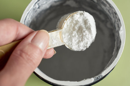 Close-up of a hand holding a spoonful of creatine powder. Sports supplement.