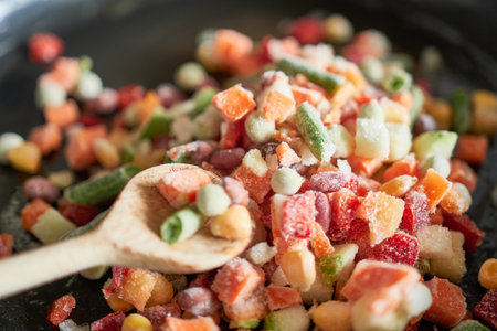 Frozen vegetables in a frying pan with a wooden spoon closeupの写真素材