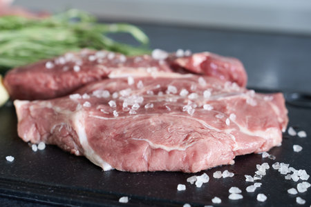 Raw fresh beef steak with salt and herbs on a black cutting boardの写真素材