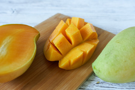 Mango fruit on a wooden board on a white wooden background.