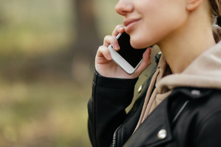 A beautiful woman in a leather jacket walks in the park and talks on the phone. A close-up planの写真素材