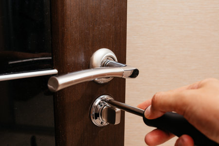 a man repairs the lock in the door of the room with a screwdriver. Repairing units on your own.の写真素材