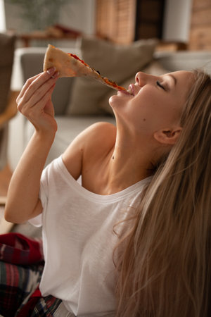 Beautiful caucasian woman in a white t-shirt eats pizza with pleasureの写真素材