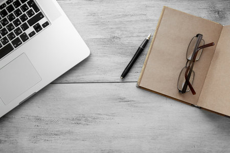 craft notebook with pen, glasses, notebook on a light wooden background top view
