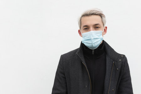 A man in a medical mask on a white background on the street looks at the cameraの写真素材