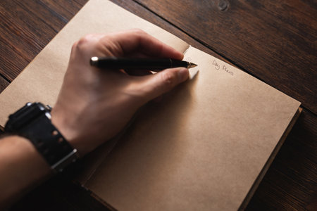 A man writes in a notebook Day plans with a pen on a dark wooden table.